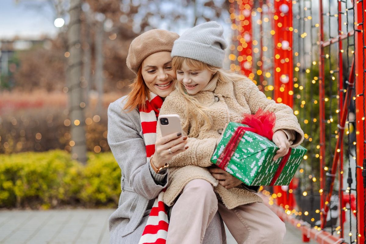 Smiling mother and her cute daughter using smartphone outdoors during Christmas holidays stock photo